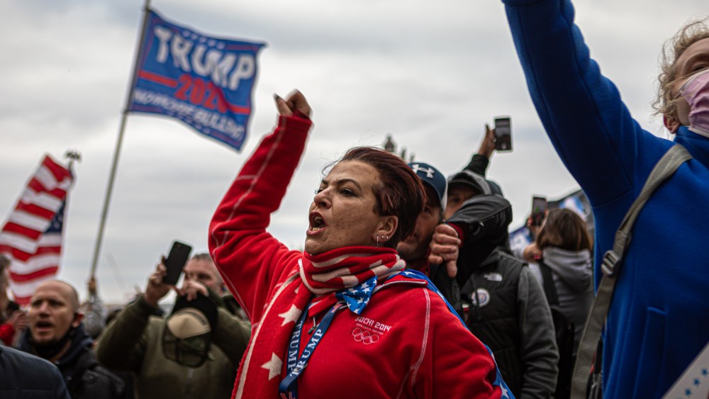 Image: A woman shouting amidst protesters waving the American flag and a flag that reads," Trump 2020".