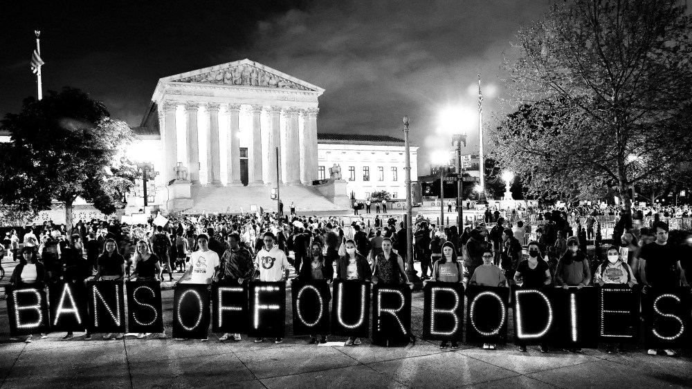 Image: Activists rallying outside the Supreme Court holding up single boards that spell out,"Bans off our bodies".