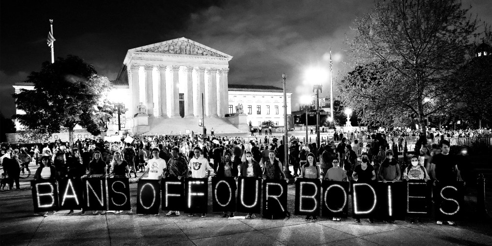Image: Activists rallying outside the Supreme Court holding up single boards that spell out,"Bans off our bodies".