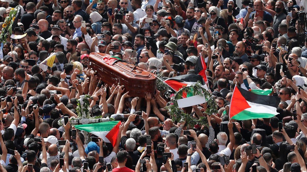 Image: Mourners wave national flags as they carry the casket during a funeral procession.