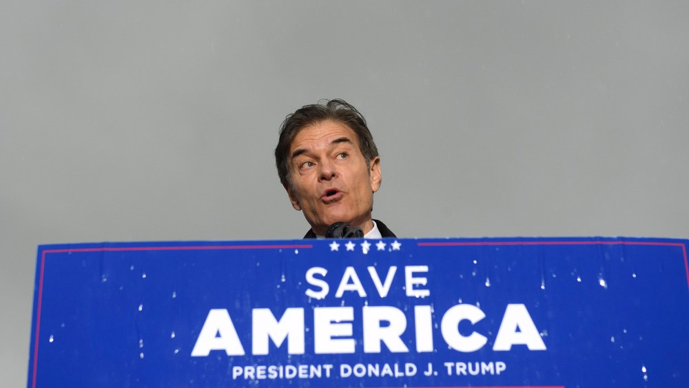 Image: Dr. Mehmet Oz standing behind a podium with a sign that reads,"Save America, President Donald j. Trump".