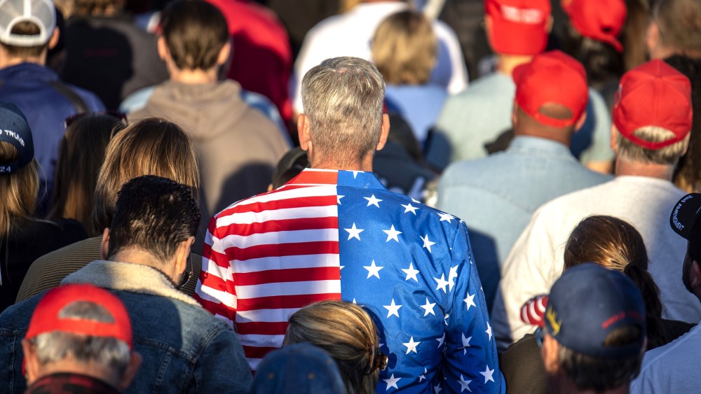 Image: Man in the centre wearing a blazer with American flag colors amidst attendees at a rally.