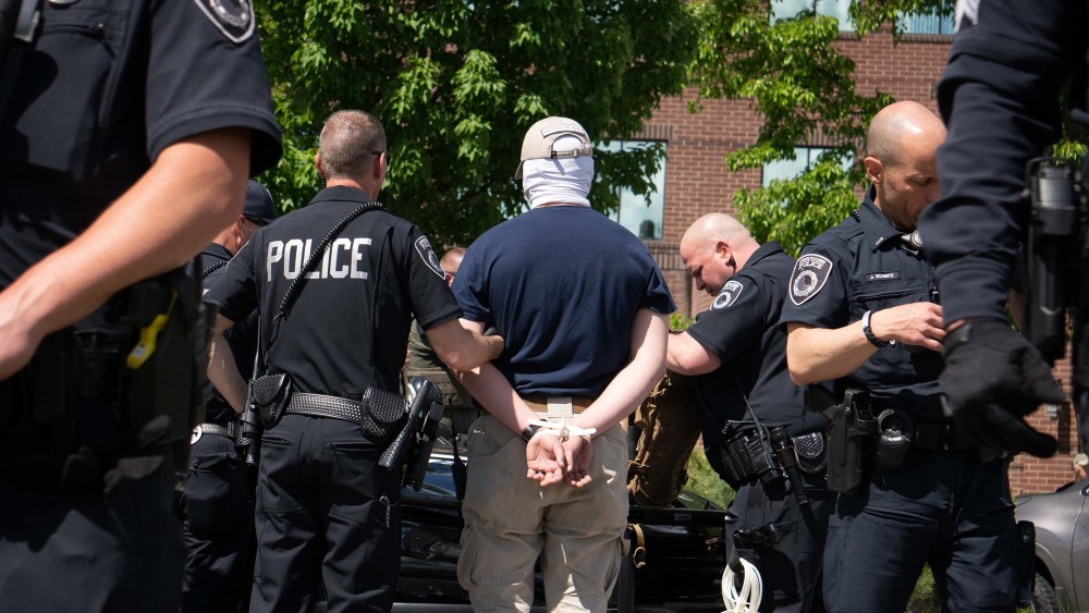 Image: Back of a person handcuffed being escorted by police officers.