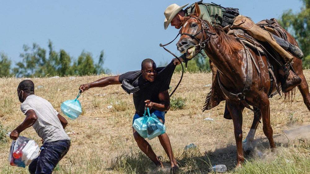 Image: A border patrol agent trying to stop a migrant carrying a food packet.