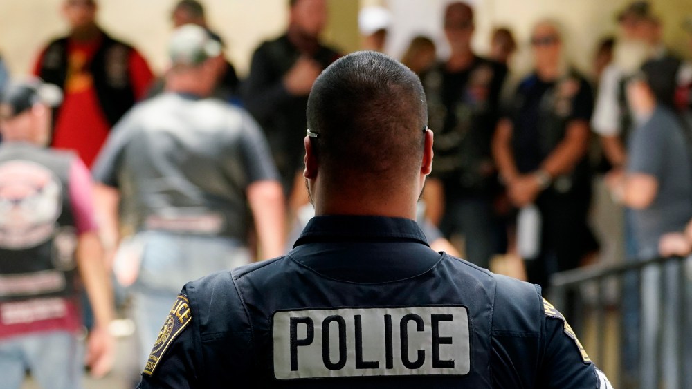 Image: Back of a police officer facing people assembling at a church.