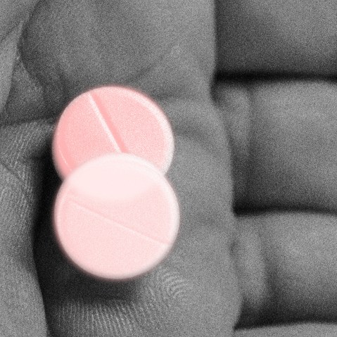 Photo illustration: A hand holding holding two pills with a light pink color overlay.