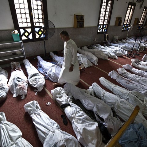 An Egyptian man walks between lines of bodies wrapped in shrouds at a mosque in Cairo on August 15, 2013, following a crackdown on the protest camps of supporters of ousted Islamist president Mohamed Morsi the previous day.  (Photo by Khaled Desouki...