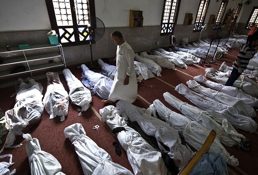 An Egyptian man walks between lines of bodies wrapped in shrouds at a mosque in Cairo on August 15, 2013, following a crackdown on the protest camps of supporters of ousted Islamist president Mohamed Morsi the previous day.  (Photo by Khaled Desouki...