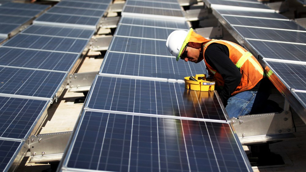 A worker finishes installing solar panels funded by federal stimulus funds atop a government building.