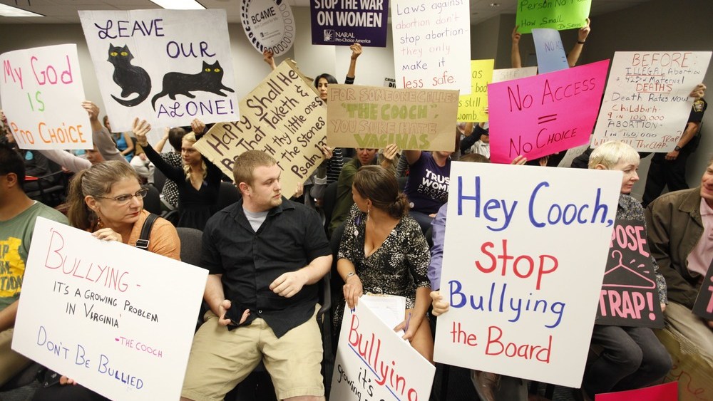 Protesters hold signs as they wait for the Virginia Board of Health meeting on abortion clinic regulations in Richmond, Va.