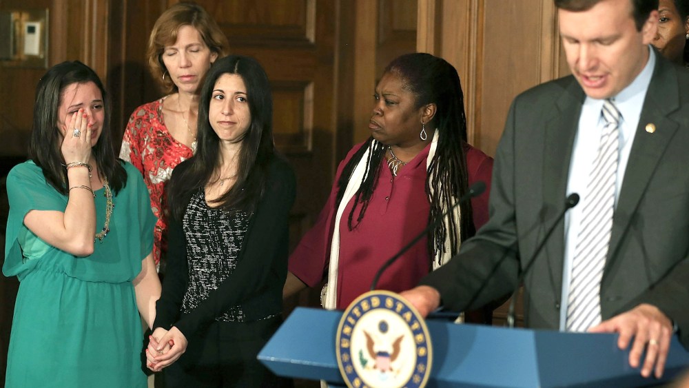 Jillian Soto (L), who lost her sister in the Newtown shooting, holds hands with Miya Rahamim, who lost her father in a unrelated shooting, as they listen to Sen. Chris Murphy, a Connecticut Democrat, read names of shooting victims during a news...