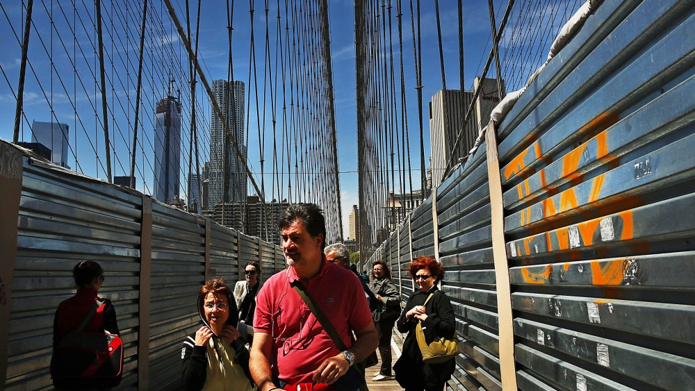 People walk past protective metal sheeting along the Brooklyn Bridge on April 30, 2013 in New York City.