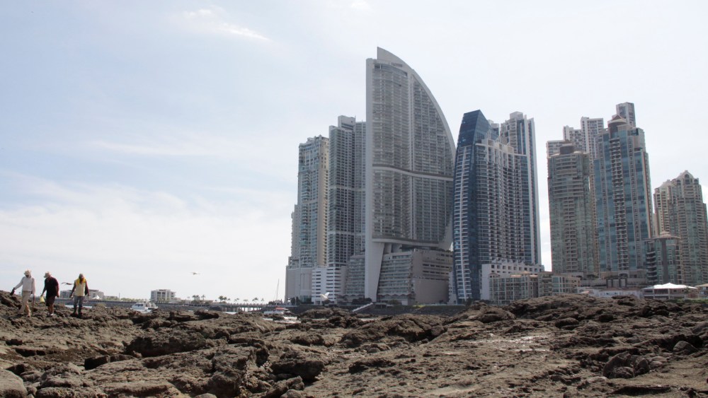Image: People stand on rocks on the shore during low tide as the Trump Ocean Club International Hotel and Tower Panama is seen next to apartment buildings in Panama City