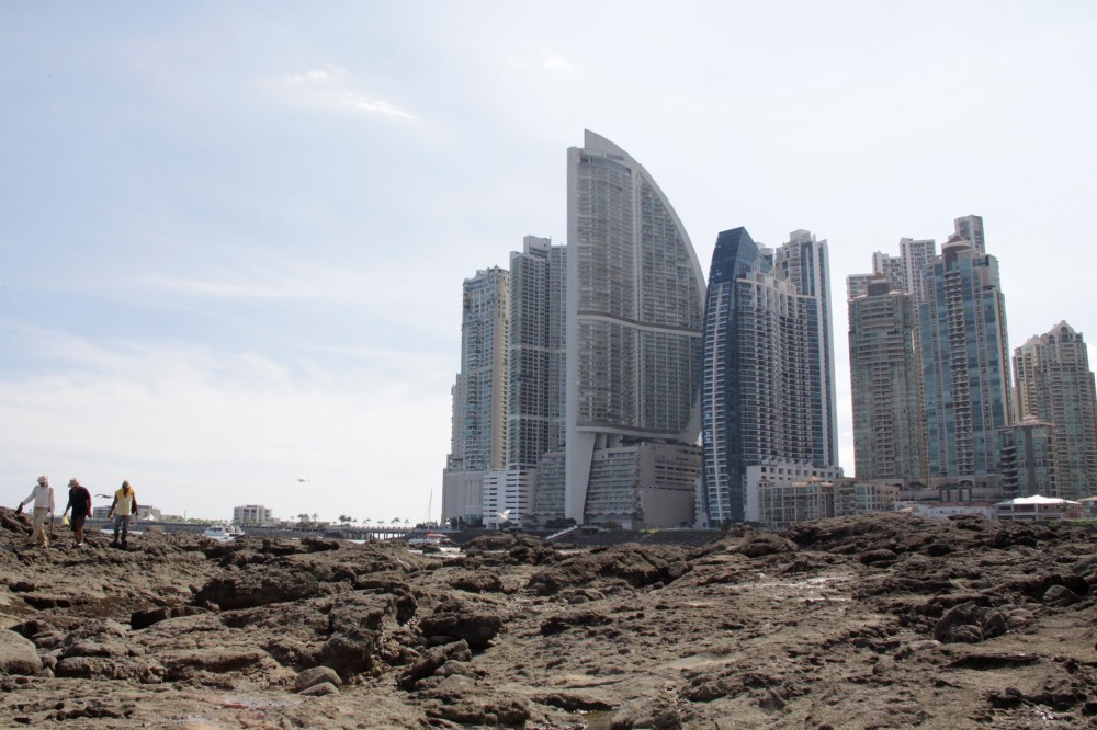 Image: People stand on rocks on the shore during low tide as the Trump Ocean Club International Hotel and Tower Panama is seen next to apartment buildings in Panama City