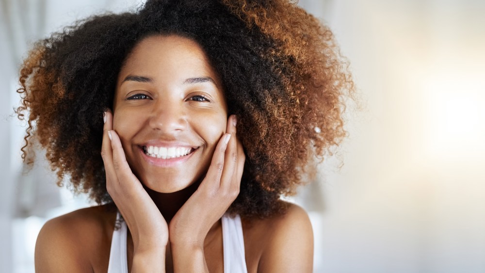 Smiling woman with curly hair. These are the 12 best natural hair products of 2021. Shop the products that will promote healthier hair growth, shine, and movement for your natural hair.