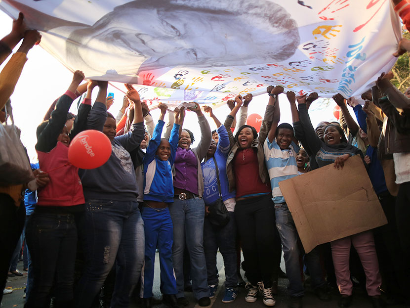 People dance and celebrate as they wave a banner of Nelson Mandela to celebrate his 95th birthday outside the Mediclinic Heart Hospital where he is being treated on July 18, 2013 in Pretoria, South Africa. (Photo by Christopher Furlong/Getty Images)