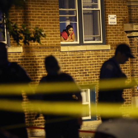 A woman watches from her window as police look for evidence after 20-year-old Carlos Barron was shot and killed in the Humboldt Park neighborhood on July 19, 2013 in Chicago, Illinois. (Photo by Scott Olson/Getty Images)