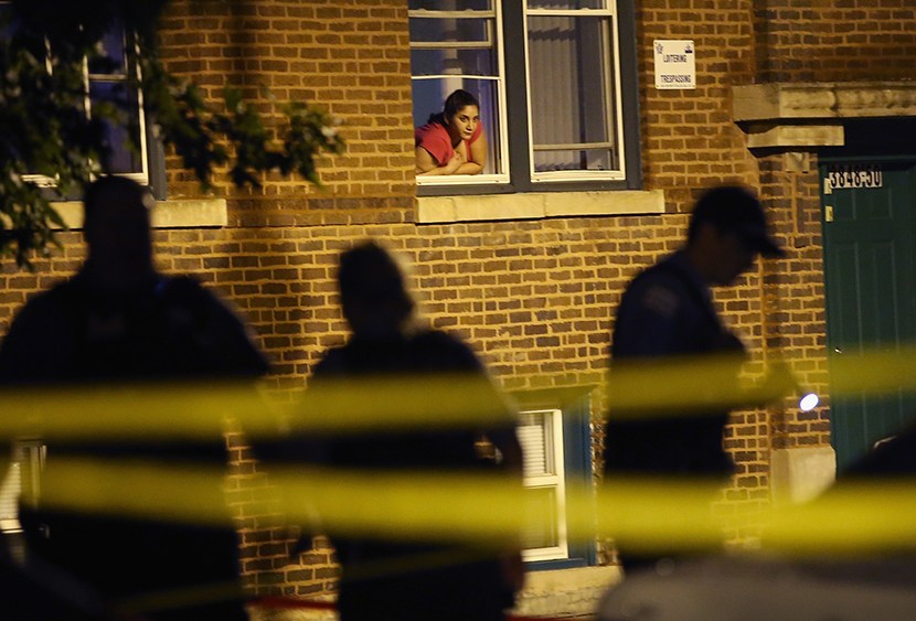 A woman watches from her window as police look for evidence after 20-year-old Carlos Barron was shot and killed in the Humboldt Park neighborhood on July 19, 2013 in Chicago, Illinois. (Photo by Scott Olson/Getty Images)