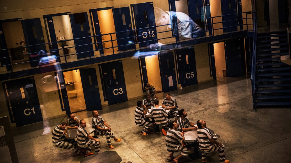An officer is reflected in the glass as inmates sit in the county jail in Williston, North Dakota, July 26, 2013.