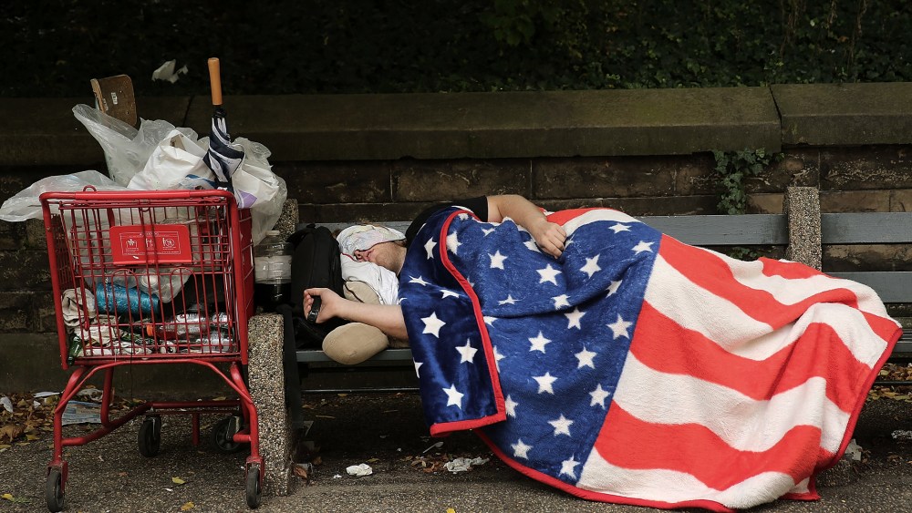 A homeless man sleeps under an American Flag blanket on a park bench on Sept. 10, 2013 in the Brooklyn borough of New York City.