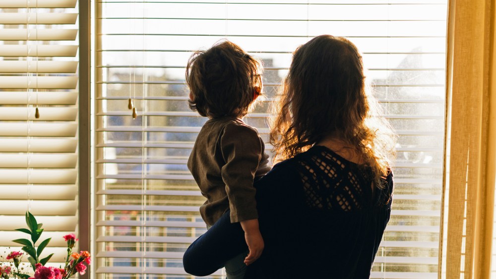 Rear View Of Mother And Baby Standing Against Window