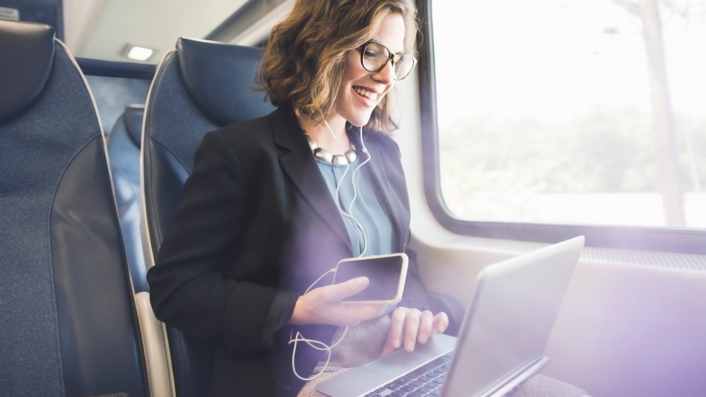 Mid adult woman on train, using smartphone and laptop
