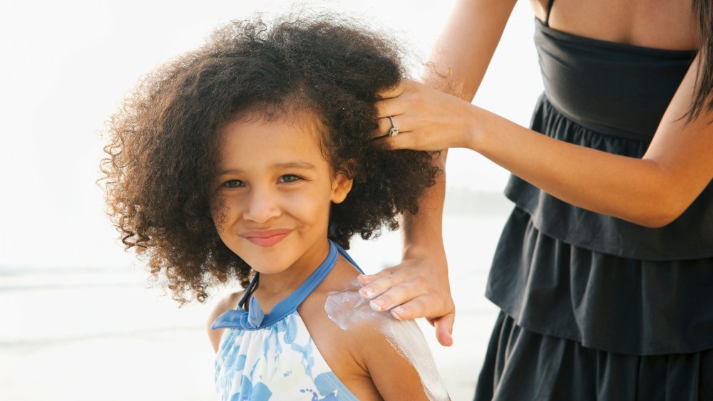 Image: Hispanic mother rubbing sunscreen on daughter at beach