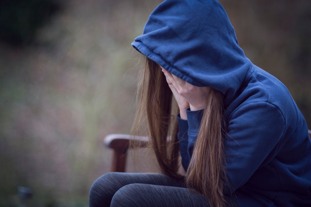 Image: Teenage girl in hooded top, with head in hands in despair