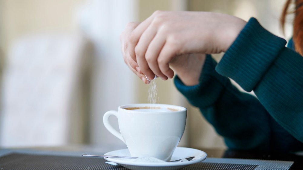 Woman pouring sugar into coffee