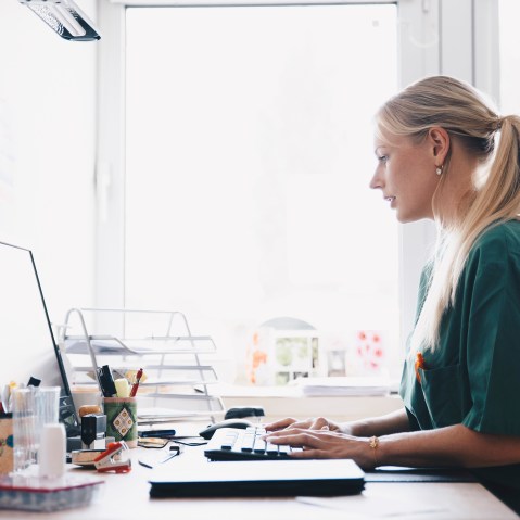 Image: Side view of female nurse working at computer desk against window in office
