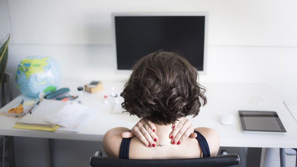 Image: Young woman massaging her neck at desk