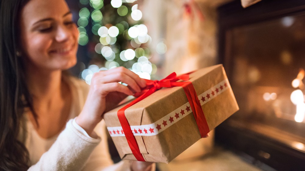 Woman in front of Christmas tree holding present.