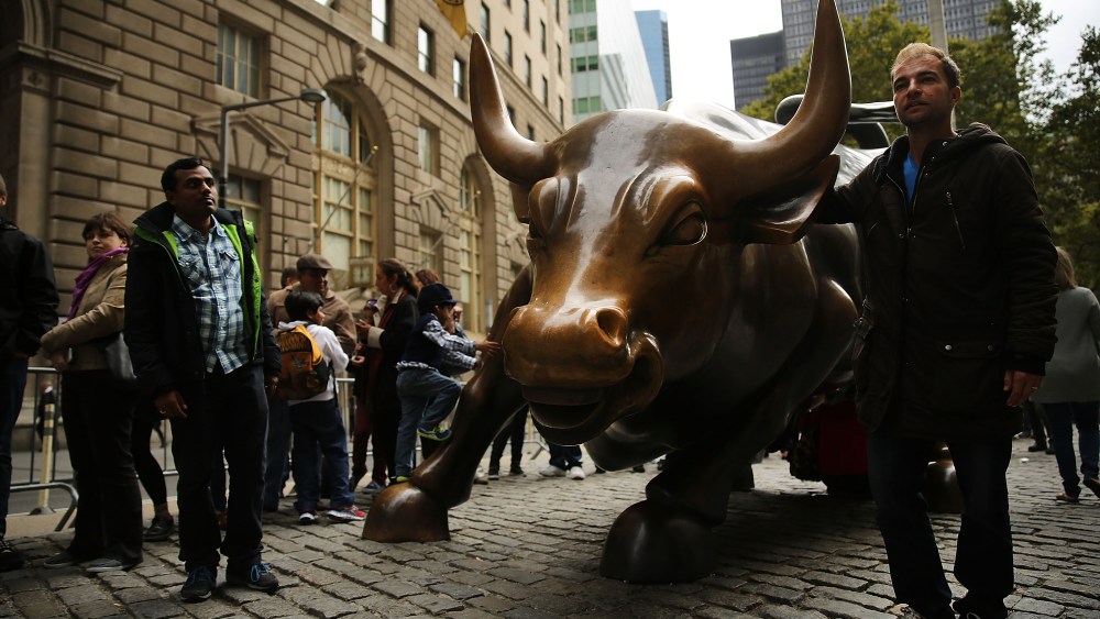 Pedestrians pass the bronze Charging Bull sculpture next to Wall Street in the Financial District on October 10, 2013 in New York City.