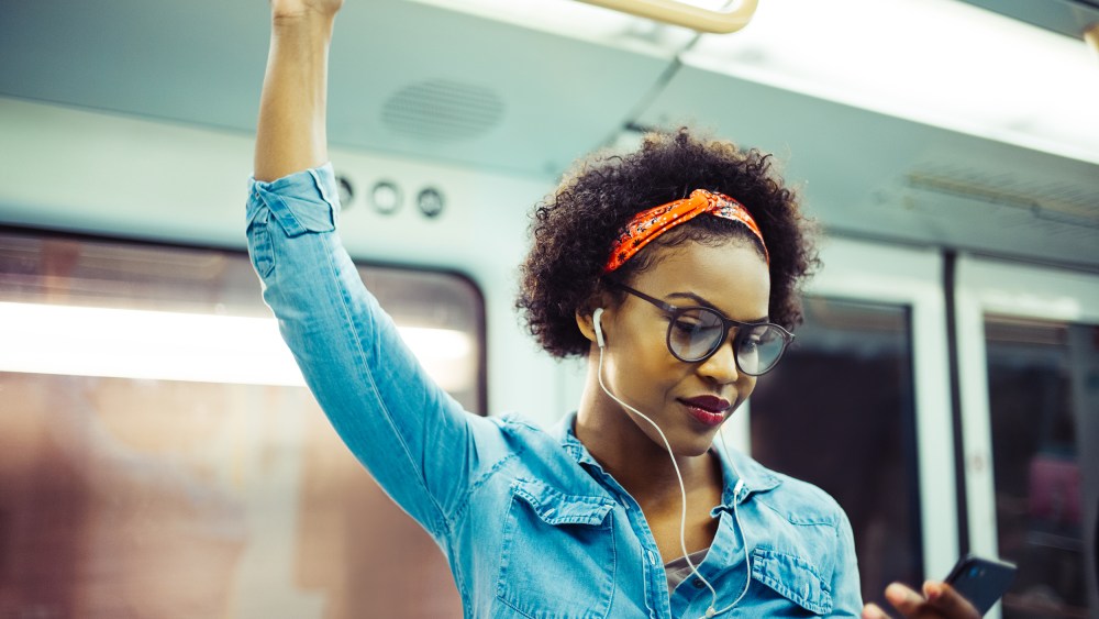 Image: Smiling young African woman listening to music on the subway