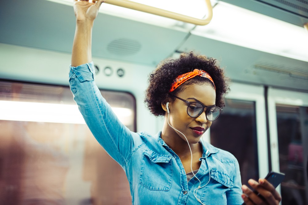 Image: Smiling young African woman listening to music on the subway
