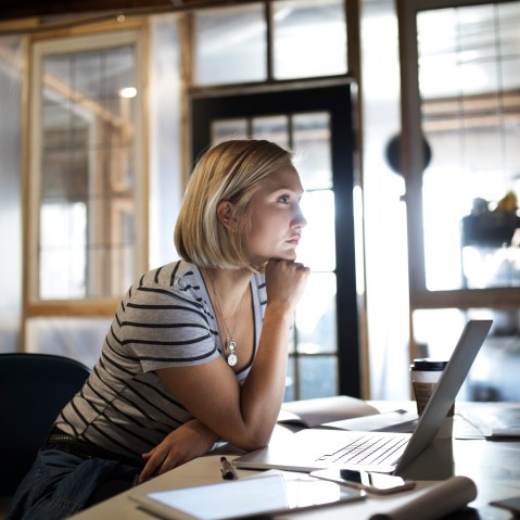 Pensive, focused woman working at laptop in office
