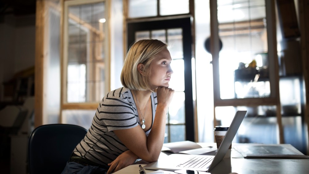 Pensive, focused woman working at laptop in office