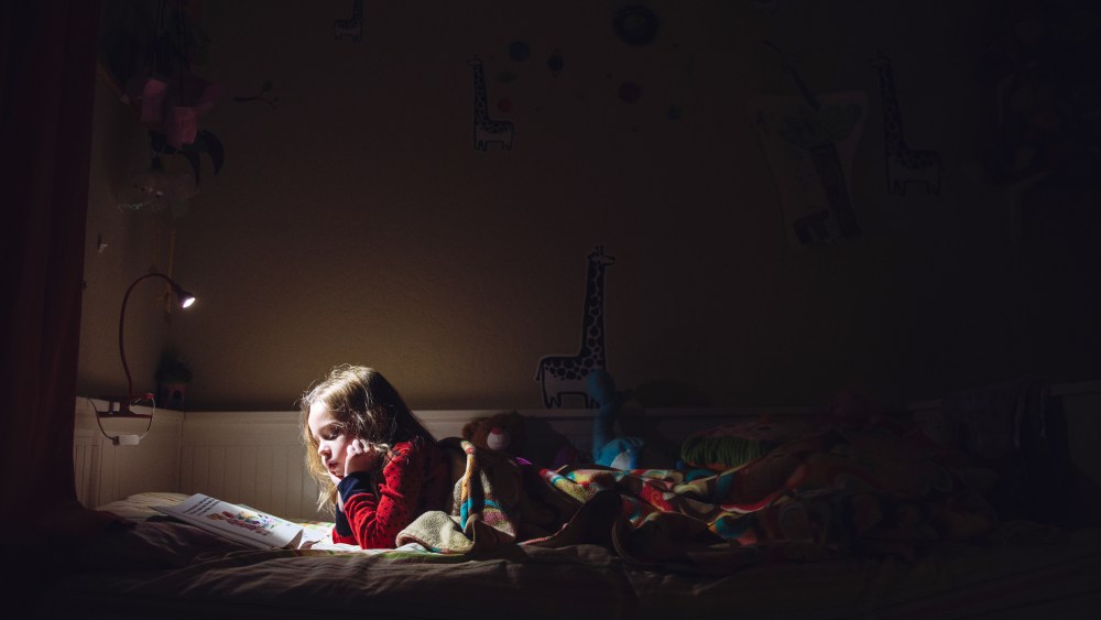 Image: A six year old girl is reading in her bed at night.
