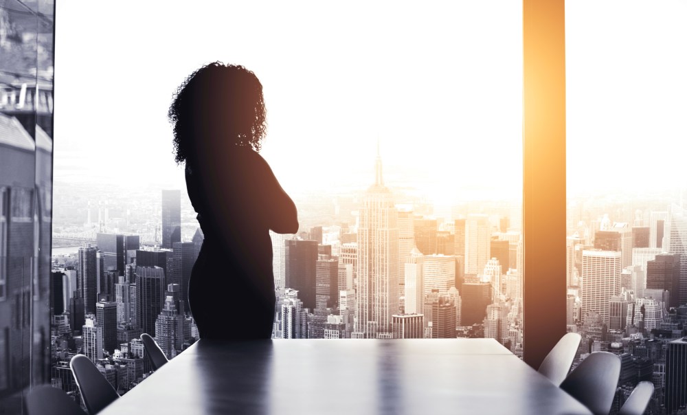 Image: Silhouetted shot of a young businesswoman looking at a cityscape from an office window