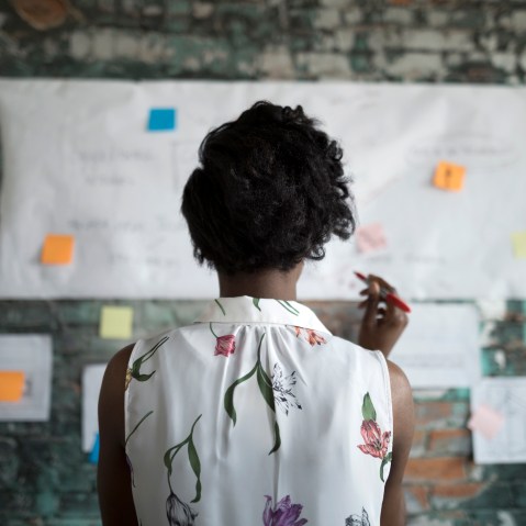 Creative businesswoman brainstorming, reviewing flow chart hanging on brick wall in office