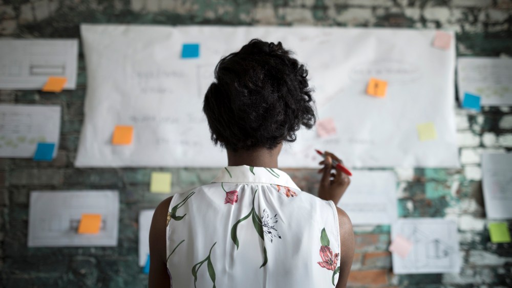 Creative businesswoman brainstorming, reviewing flow chart hanging on brick wall in office
