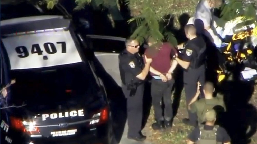 Image: A man placed in handcuffs is led by police near Marjory Stoneman Douglas High School following a shooting incident in Parkland