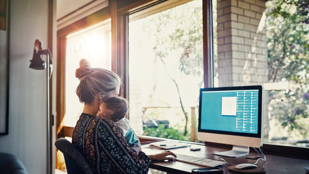 young woman working at home while holding her newborn baby son