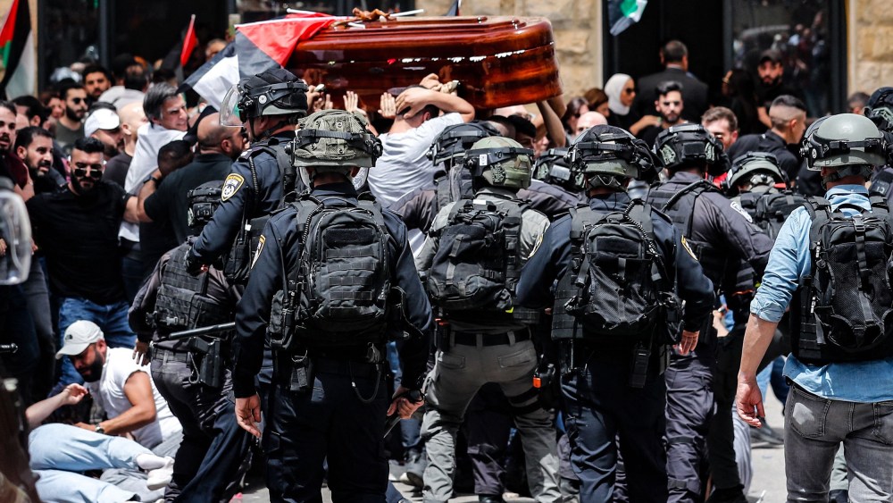 Image: Security forces and clash with mourners carrying a casket and Palestinian flags.