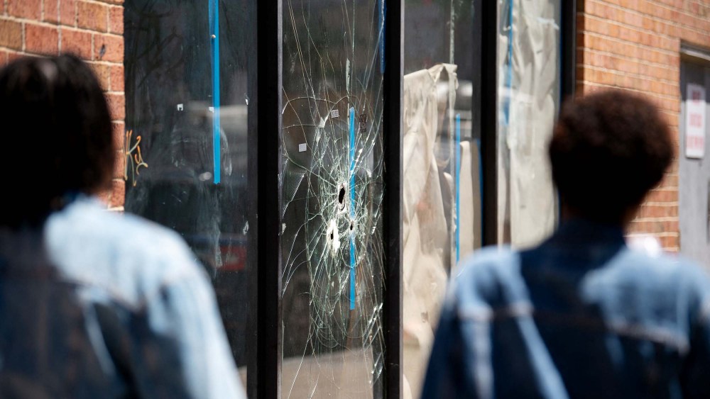 Pedestrians walk past bullet holes in the window of a store front on South Street in Philadelphia, Penn. on Sunday.