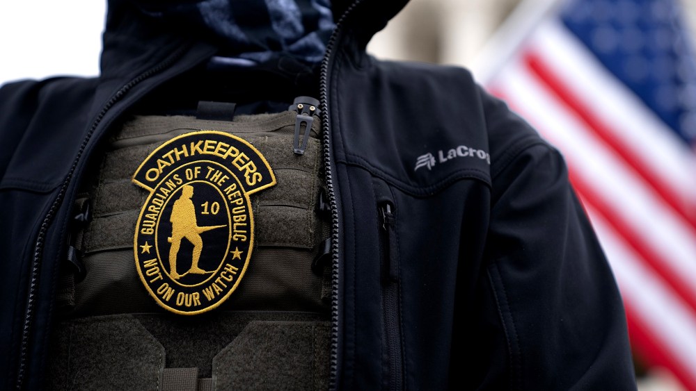 Image: A demonstrator wearing a badge over a protective vest that reads,"Oath Keepers. Guardians of the Republic. Not on our watch."