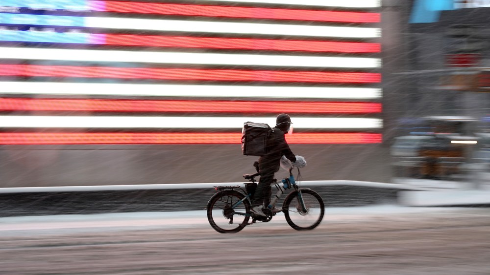 Image: A food delivery guy on a bicycle is seen as snowfall blankets the Times Square in New York City.