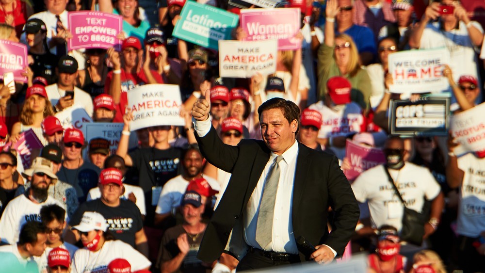 Image: Ron DeSantis speaks to a crowd during a campaign rally. A sign in the audience reads,"Latinos for Trump".