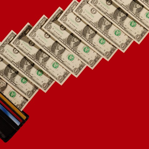 Image: Man's hands holding wallet with one dollar bills ascending diagonally on a red background.