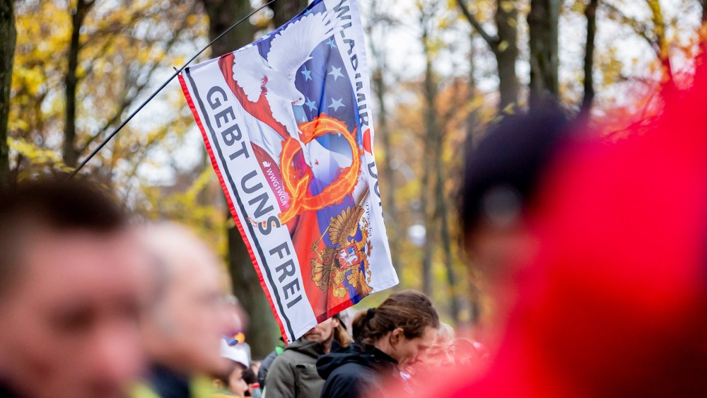 Image: A flag of the "QAnon" movement at a demonstration against the corona restrictions of the German government at the Brandenburg Gate in Berlin. The flag reads,"GEBT UNS FREI".
